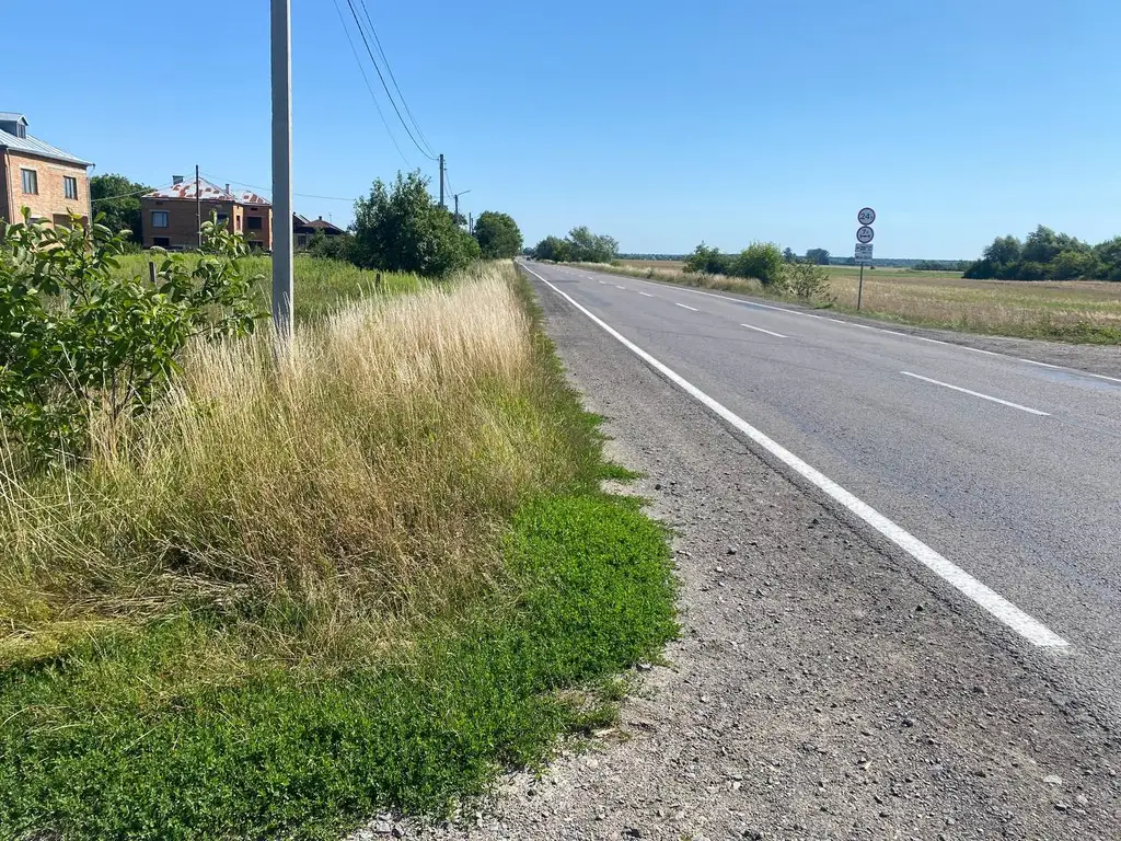 Асфальтована дорога з розміткою вздовж фронту ділянки, електроопора на межі, будинки сусідів